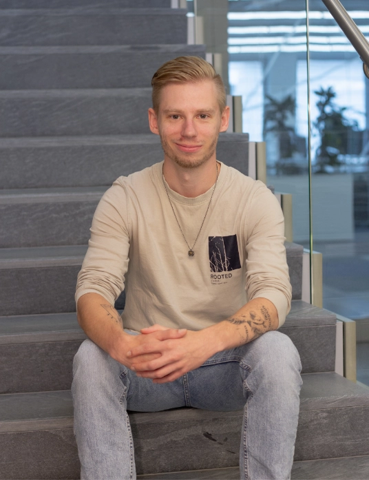 Tijmen Rothe sitzt auf einer Steintreppe, trägt ein helles Longsleeve und blickt freundlich in die Kamera