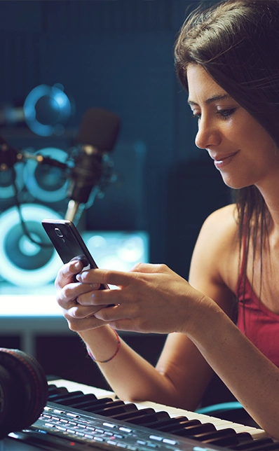 Eine junge Frau sitzt an einem Keyboard und erstellt mit dem Smartphone eine Rechnung.