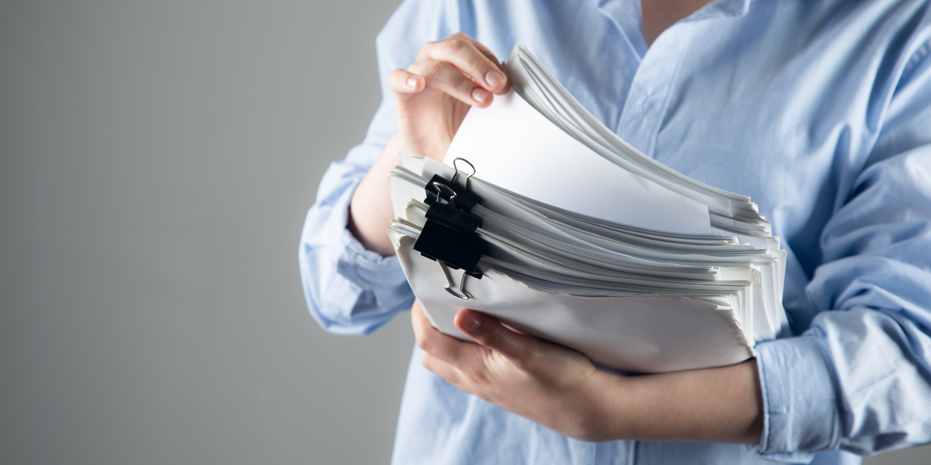 Nahaufnahme von Händen, die in einem Aktenordner mit zahlreichen Papierdokumenten und Akten blättern