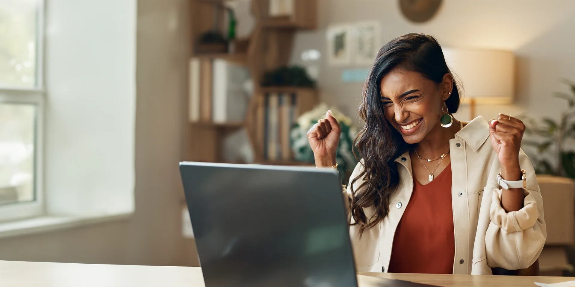 Eine Frau sitzt vor einem Laptop und freut sich über einen Erfolg.